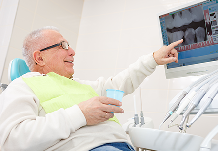 Älterer Mann auf Zahnarztstuhl in Praxis, der Röntgenbilder seines Gebisses betrachtet